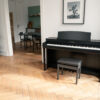 Piano numérique noir dans salon moderne avec parquet, plantes en pot et décor mural.
