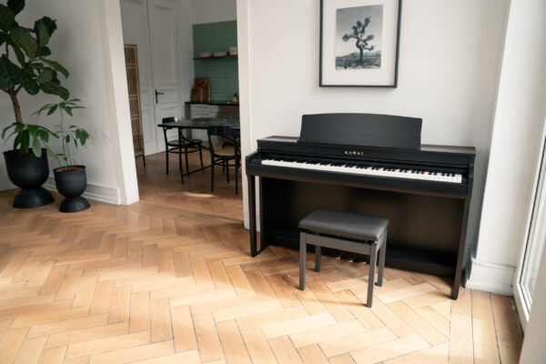 Piano numérique noir dans salon moderne avec parquet, plantes en pot et décor mural.
