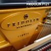 Gros plan sur l'intérieur doré d'un piano droit neuf Fridolin Schimmel, avec le numéro de série 118975 visible au centre de l'image.