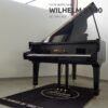 Un piano à queue noir Wilhelm WV180 dans une pièce, avec un tapis noir marqué "Au service de tous". Numéro de série 019.759.