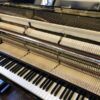 Intérieur d'un piano droit avec vue sur le clavier et le mécanisme des marteaux, illustrant la complexité de l'instrument.