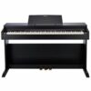 Un piano numérique noir de marque Casio, avec trois pédales et un support de partition intégré, est placé contre un mur blanc.