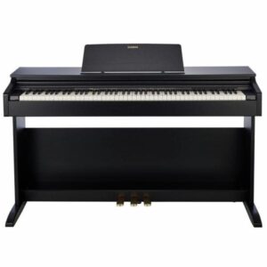 Un piano numérique noir de marque Casio, avec trois pédales et un support de partition intégré, est placé contre un mur blanc.