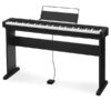 Un piano numérique noir avec support, pédale et porte-partition, posé sur une surface blanche. Aucune personne, monument ou bâtiment visible.