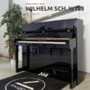 Un piano droit noir brillant, marqué "WILHELM SCH. W123", se trouve dans une pièce moderne décorée d'une plante en pot à gauche.